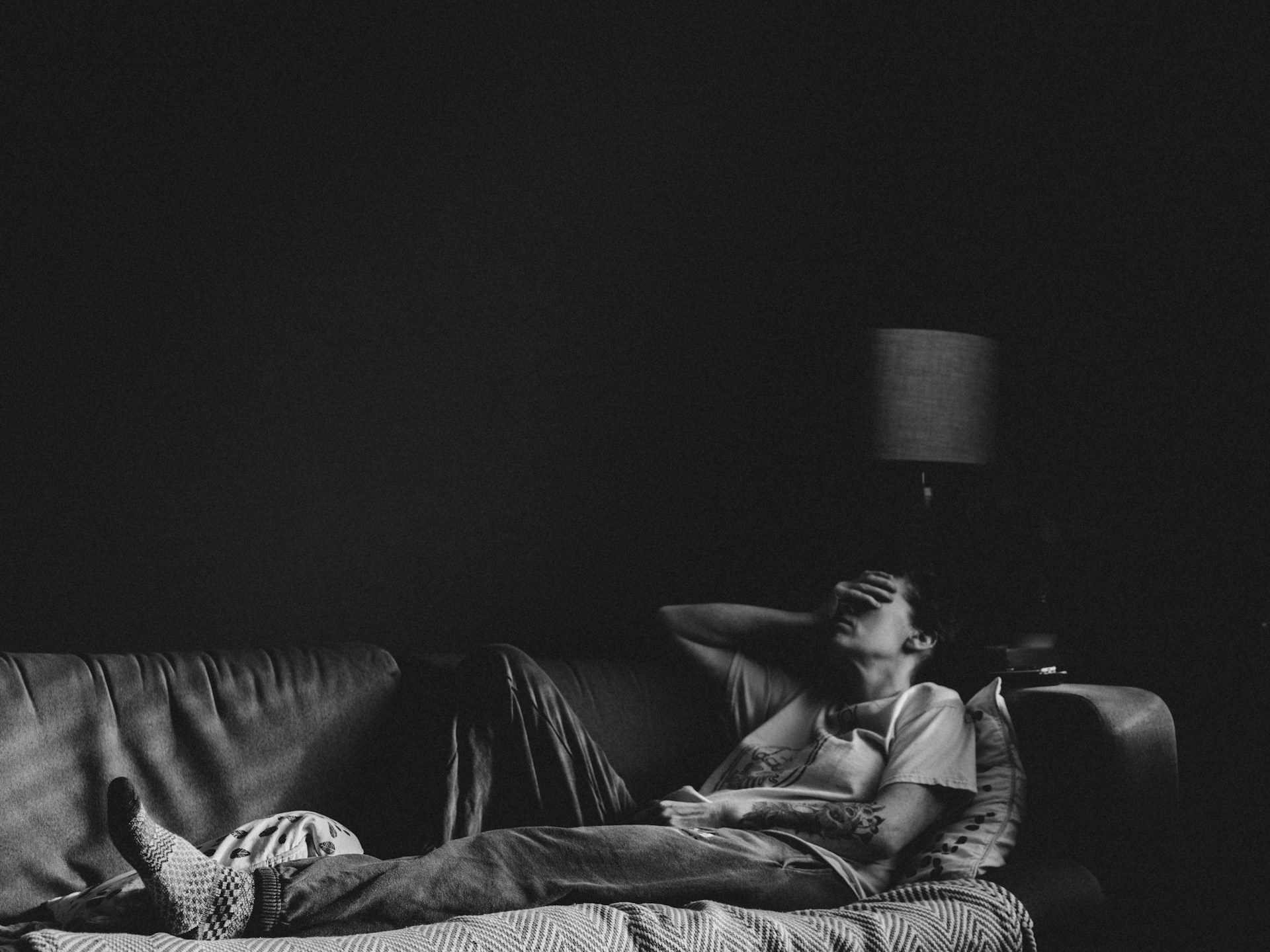 A sad person lying on the couch, covering their face with their palm